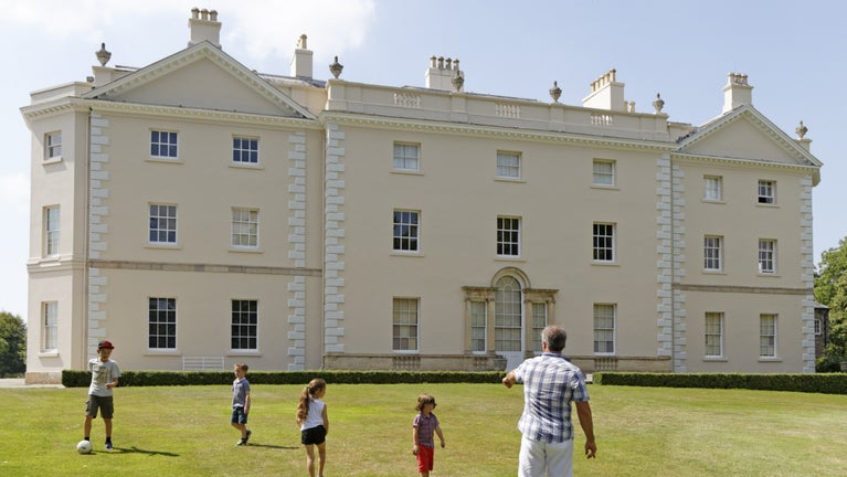 Family playing football on the grass in front of the house at Saltram